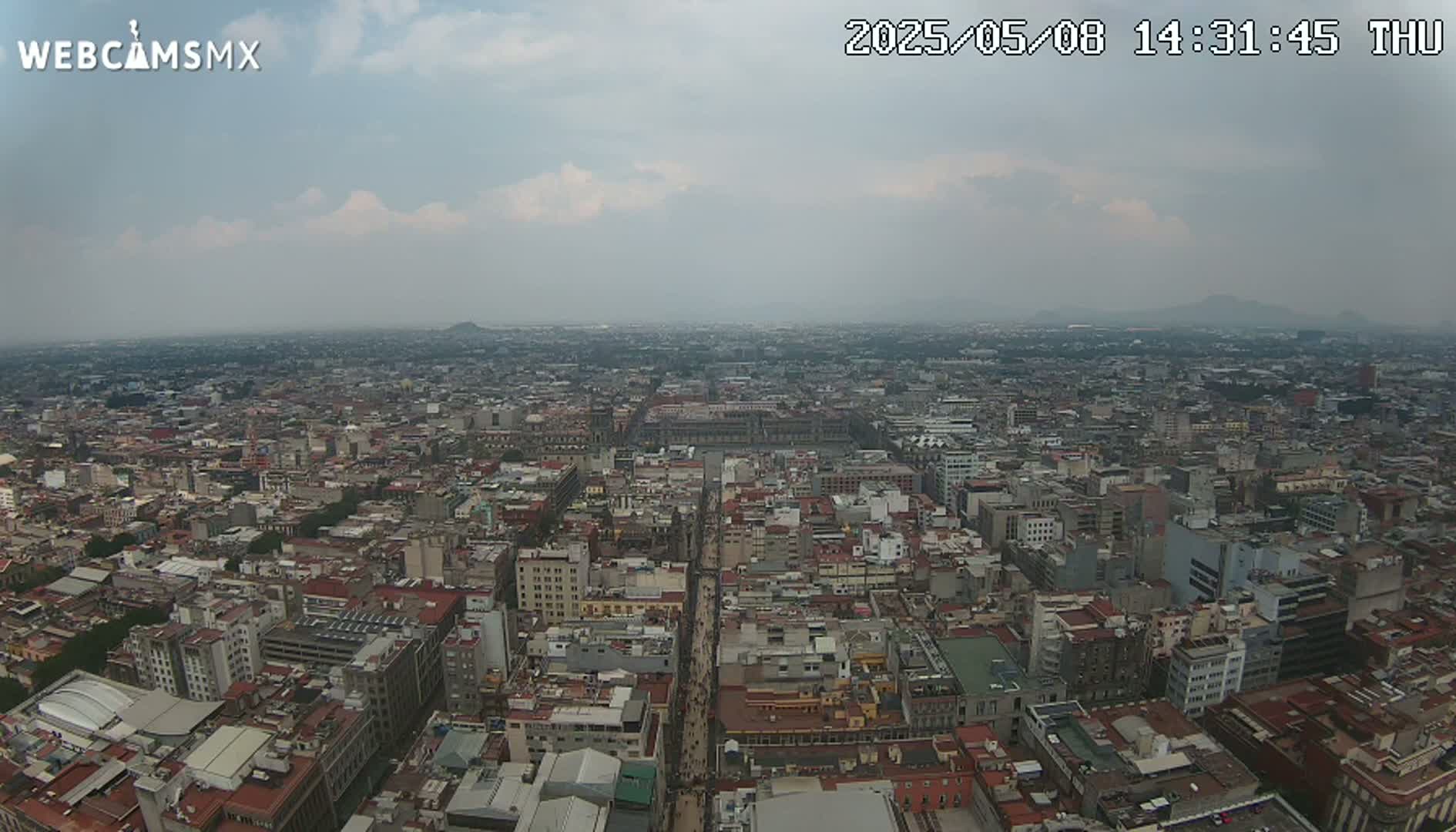 A hazy, overcast day reveals a sprawling cityscape of densely packed buildings extending to the horizon, with distant mountains barely visible.