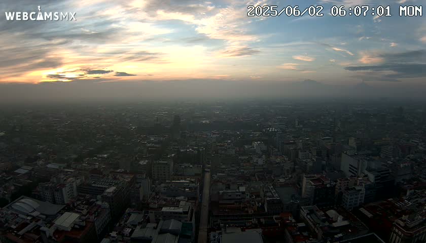 A hazy sunset casts a warm glow over a sprawling city viewed from a high vantage point.