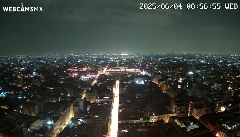 A nighttime aerial view of a sprawling city with brightly lit streets and buildings under a mostly clear sky.