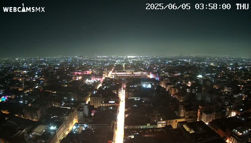A nighttime aerial view of a sprawling city with brightly lit streets and buildings under a clear, dark sky.