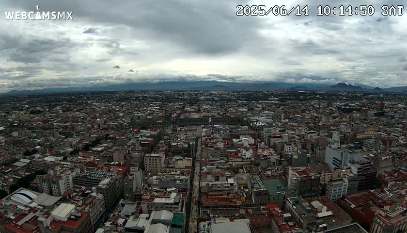 A sprawling cityscape under a cloudy sky stretches to distant mountains.