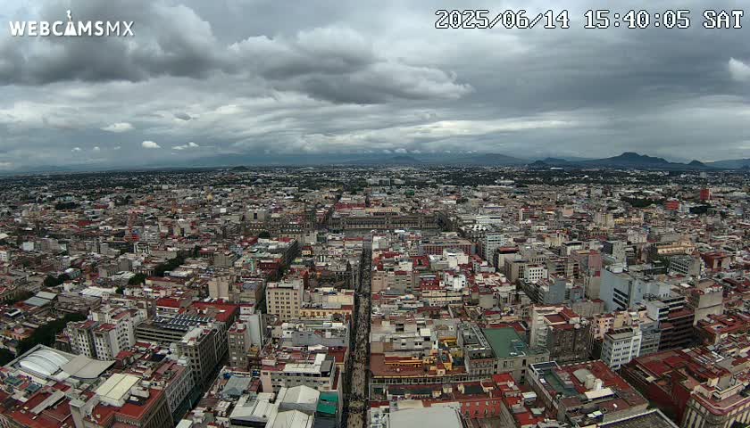 A sprawling cityscape under a cloudy sky stretches to distant mountains.