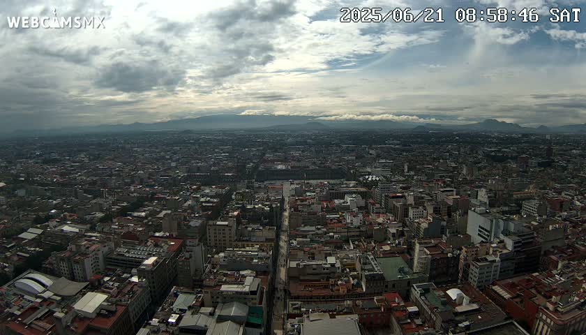 An expansive view of a city under a cloudy sky shows a vast cityscape stretching to distant mountains.