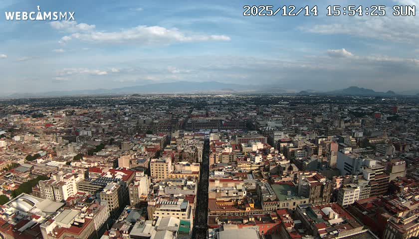 An expansive nighttime panoramic view reveals a sprawling city illuminated by countless lights under a clear, dark sky, with a brightly lit central avenue leading toward a prominent building.