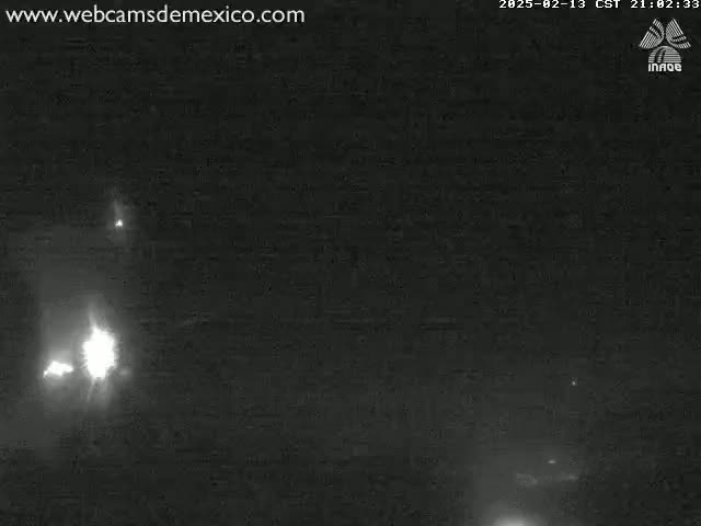 A nighttime, low-light image shows two bright lights in the distance, likely headlights, against a dark, possibly slightly hazy, sky.