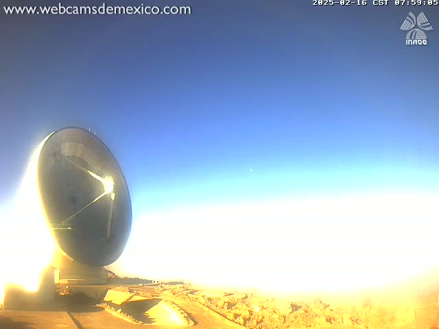 A large, round radio telescope sits in a desert landscape under a clear, bright blue sky.