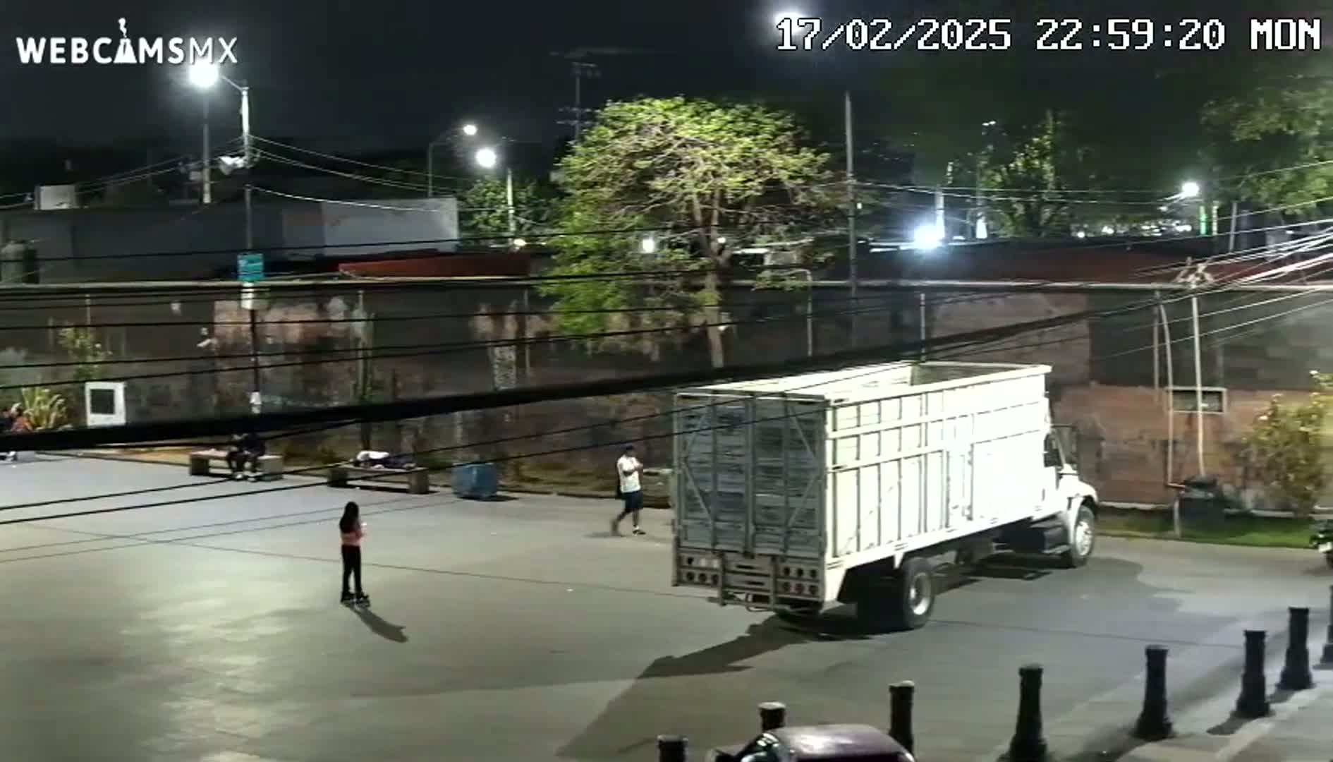 A white truck is parked in an empty nighttime parking lot next to several people, one of whom is rollerblading.