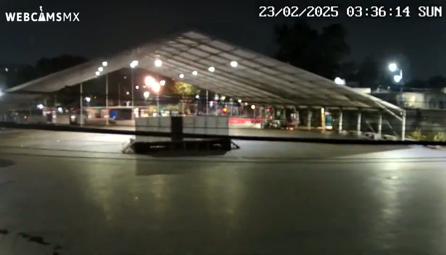 A large, open-air structure with lights is illuminated at night, with a flat, dark surface in front of it.