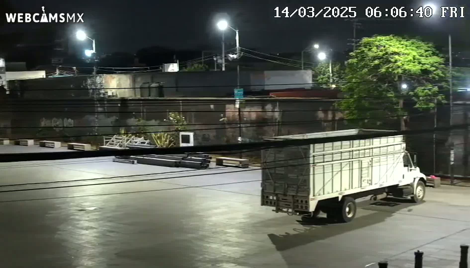 A large, white, enclosed-bed truck is parked in a paved, empty lot at night under bright artificial lights.