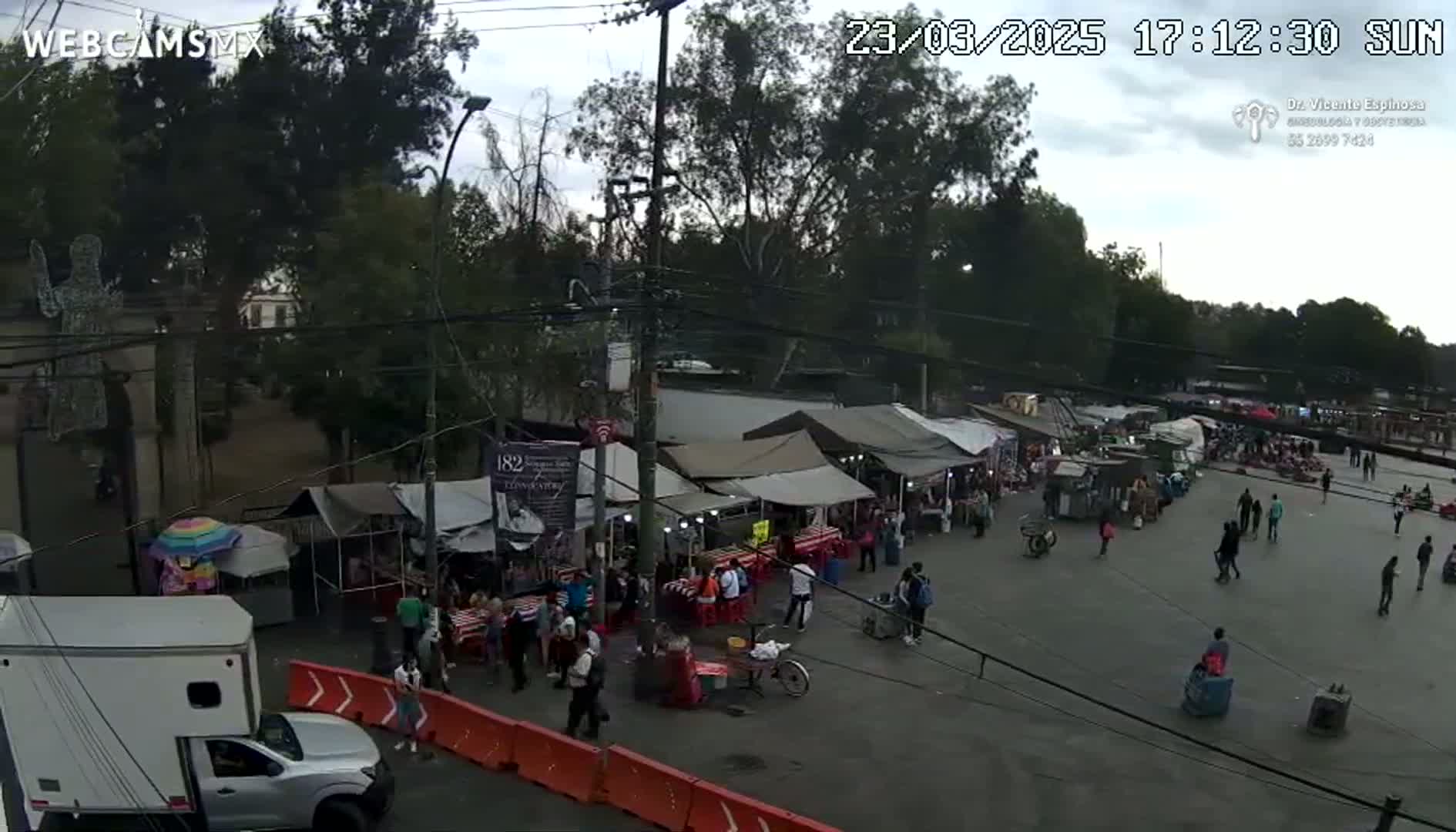 An outdoor market with numerous tents and people, under an overcast sky in the late afternoon.