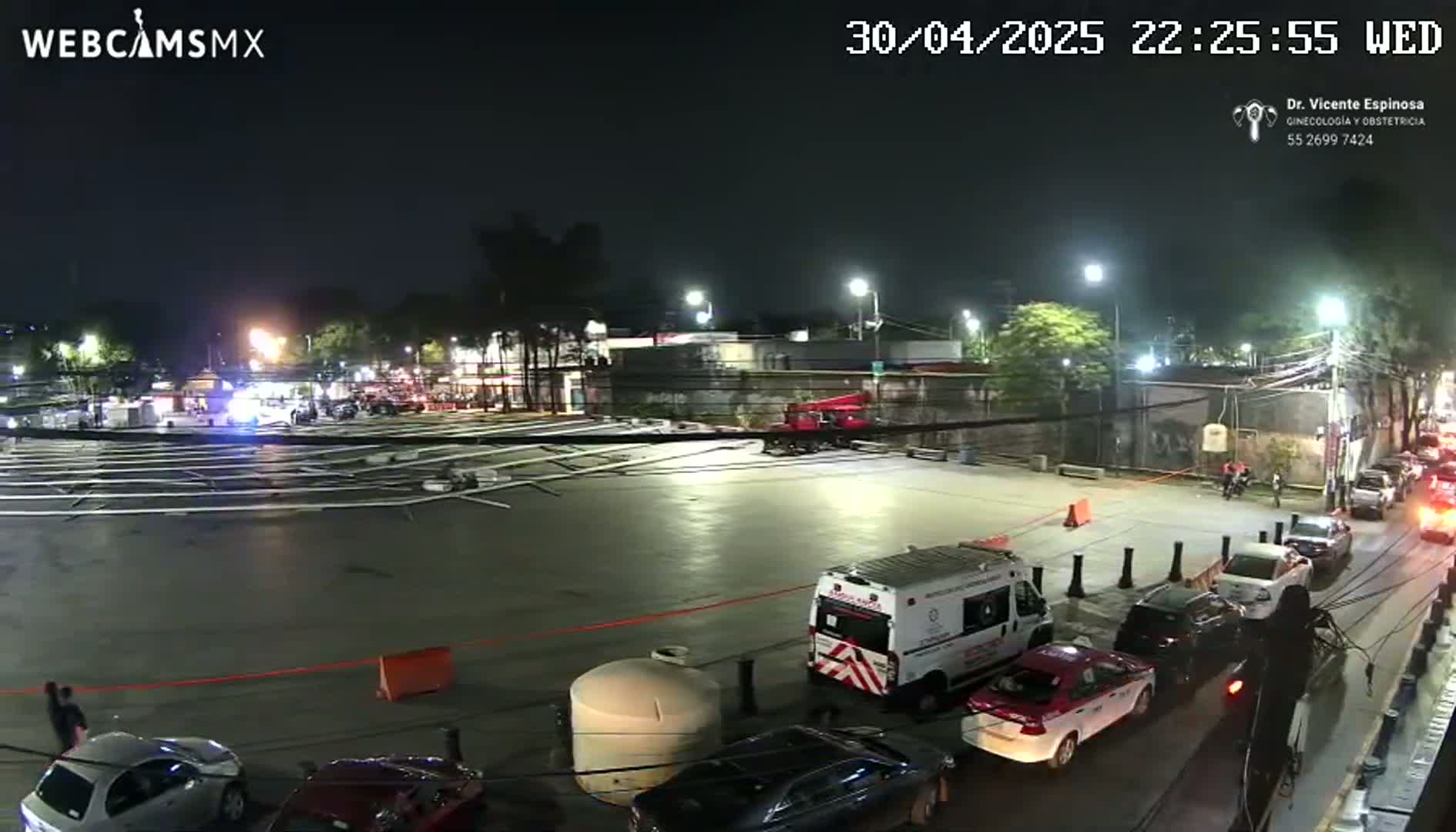 At night, a mostly empty parking lot contains scattered metal poles and several cars, with a medical van parked nearby.
