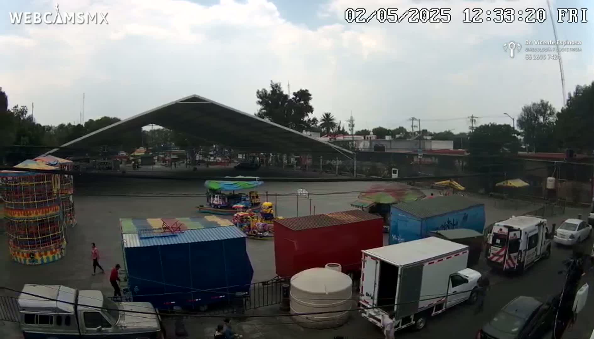 A fairground with several carnival rides and food stalls is visible under a partly cloudy sky, with numerous trucks and cars parked nearby.