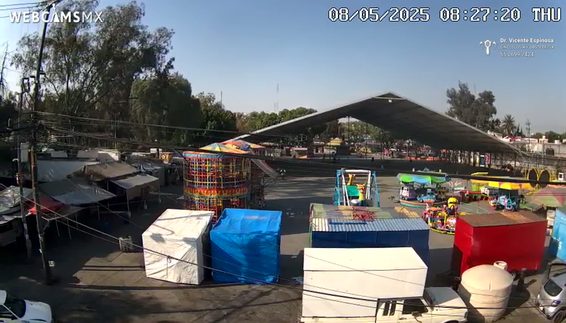 A fairground with several carnival rides and vendor stalls is visible under a sunny sky.