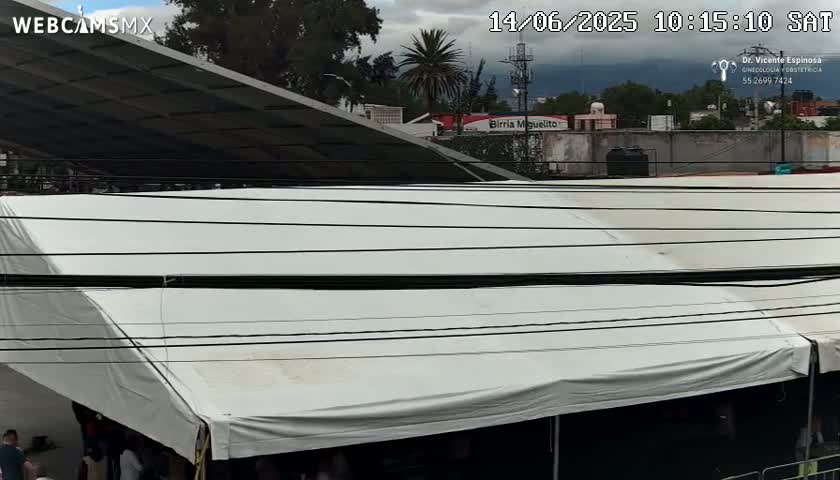 A large white tent is situated under an overhanging structure, with a partly cloudy sky visible in the background.