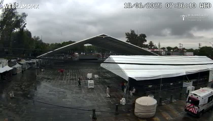 A wet, paved area with several tents and a large covered structure under an overcast sky.