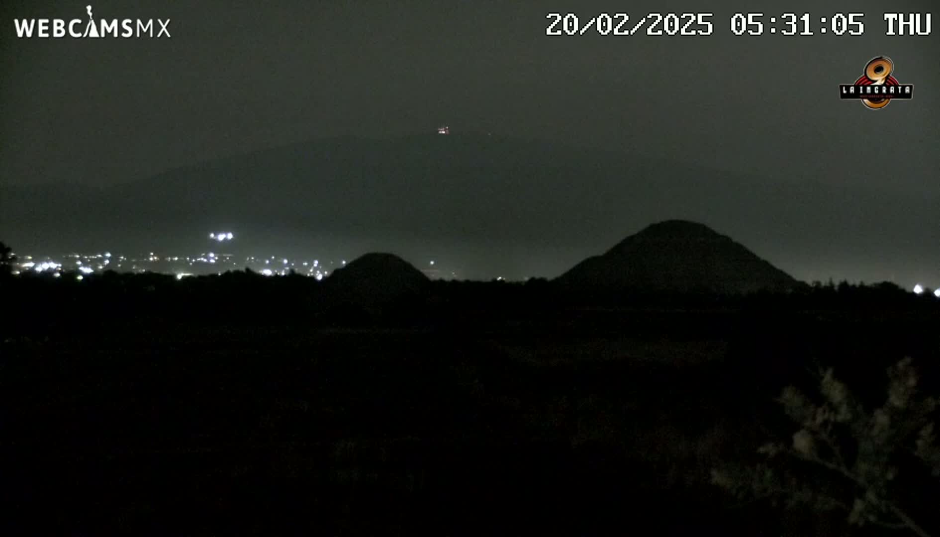 A nighttime view of dark, silhouetted hills and a distant city skyline under a cloudy, dark sky.