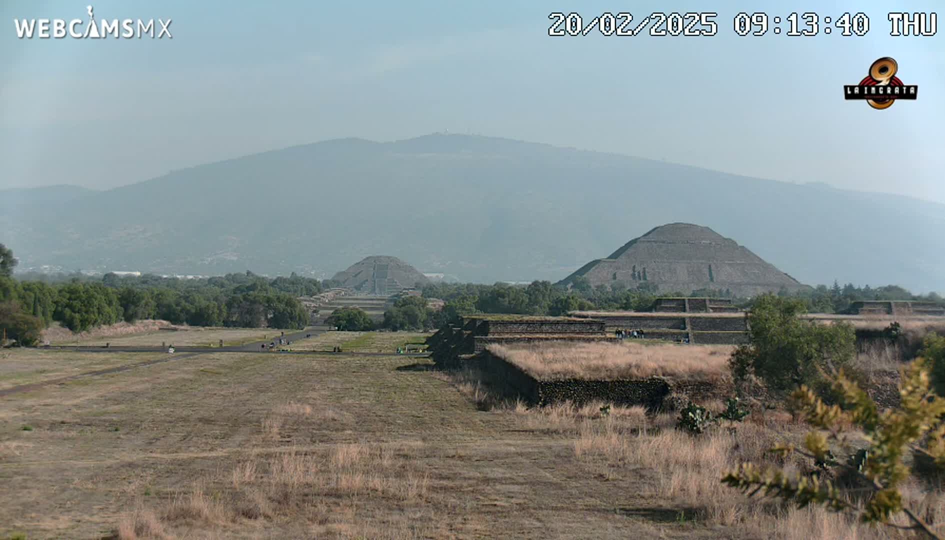 A hazy view of ancient pyramids and structures, set against a backdrop of distant mountains under a clear sky.