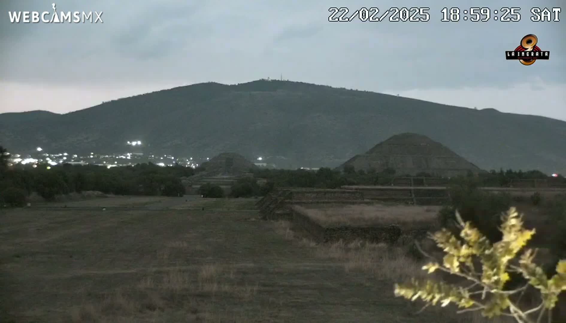 A twilight view shows several ancient stone pyramids and a distant mountain range under an overcast sky.
