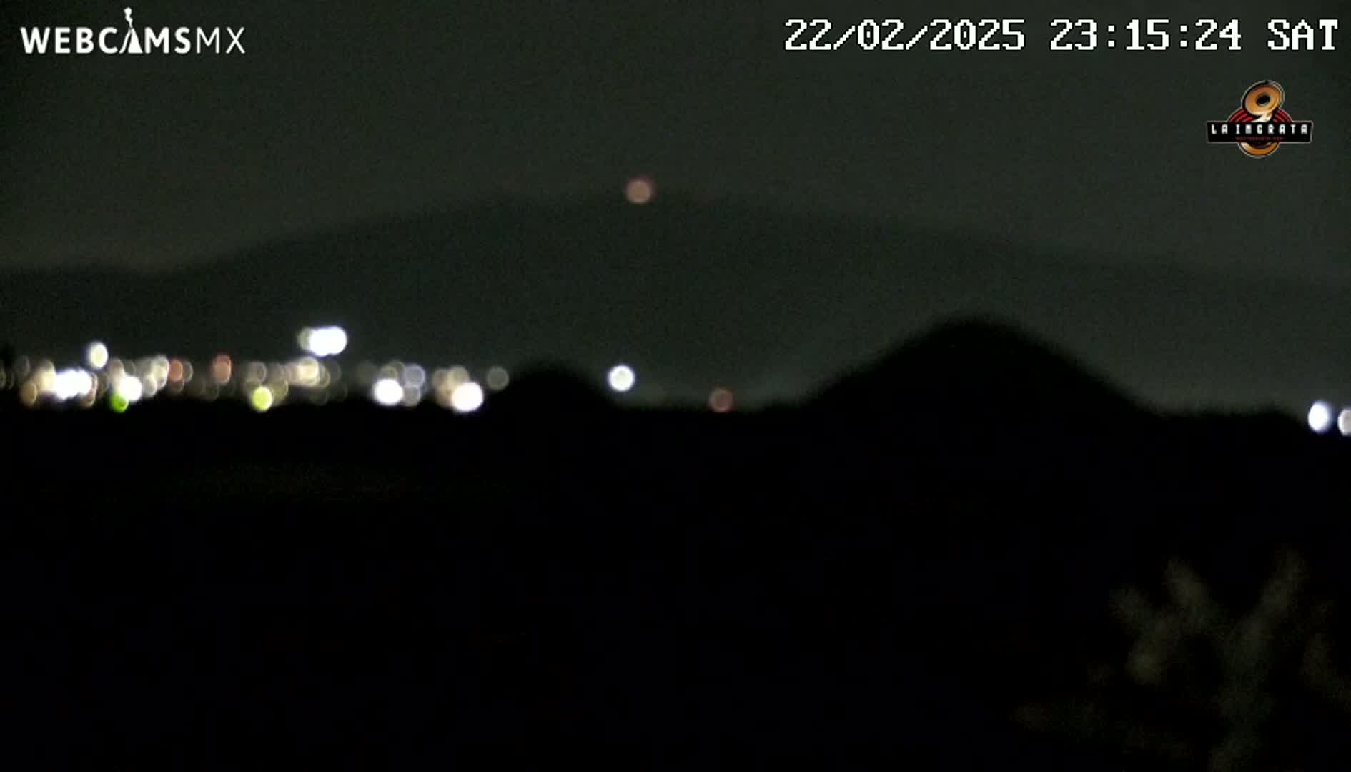 A nighttime, blurry view shows a distant city's lights and a dark, silhouetted landscape under a clear sky.