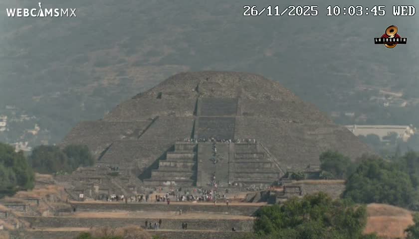 A large, dark silhouette of a pyramid dominates the foreground under a clear night sky, flanked by the scattered lights of a distant city.