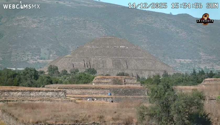 A large, dark silhouette of a pyramid dominates the foreground under a clear night sky, flanked by the scattered lights of a distant city.