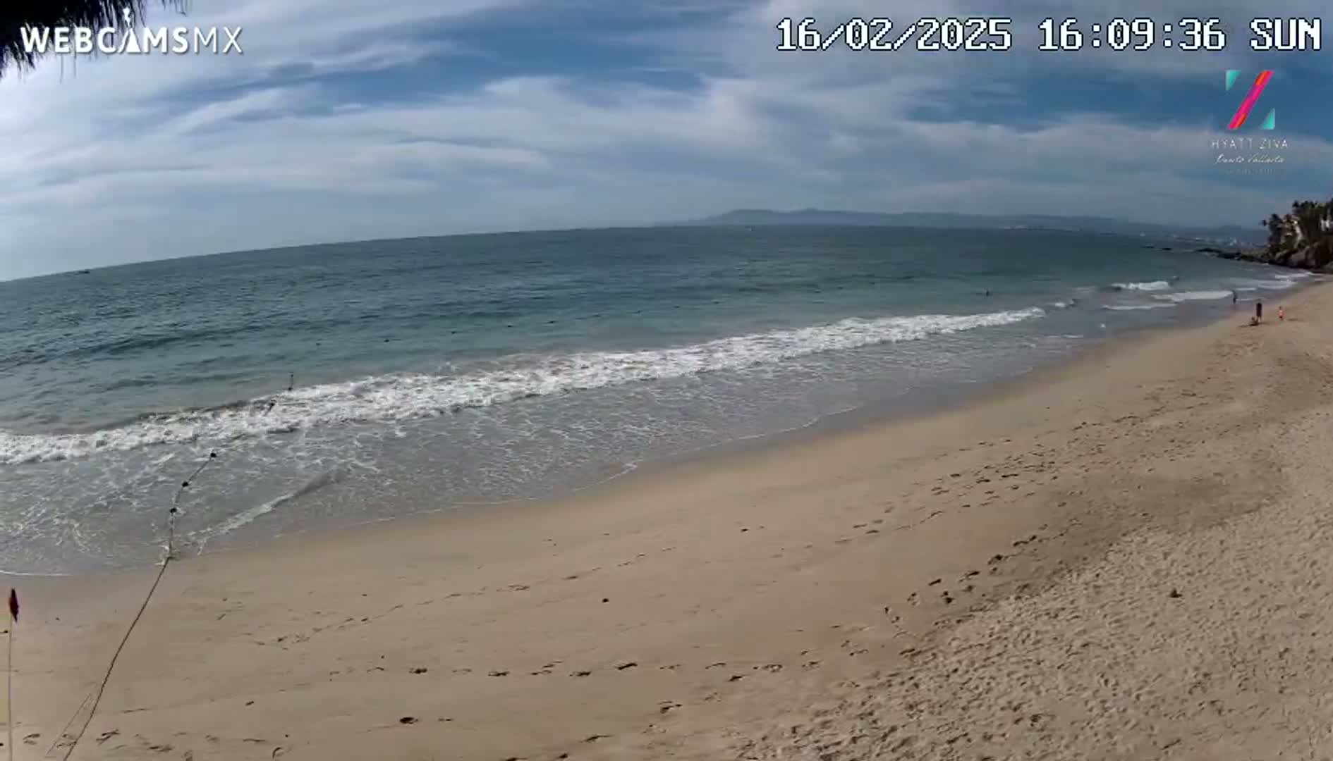A sandy beach with gentle waves under a partly cloudy sunny sky.