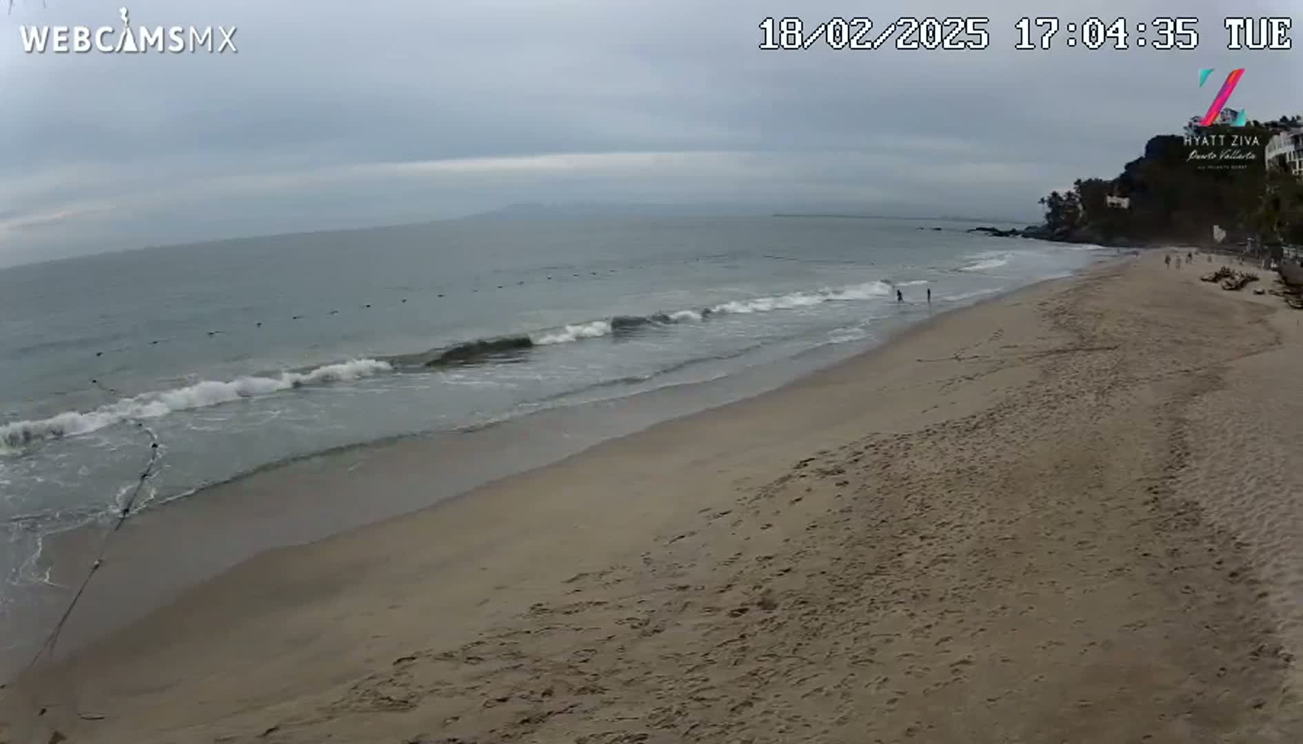 A sandy beach with gentle waves under an overcast sky.