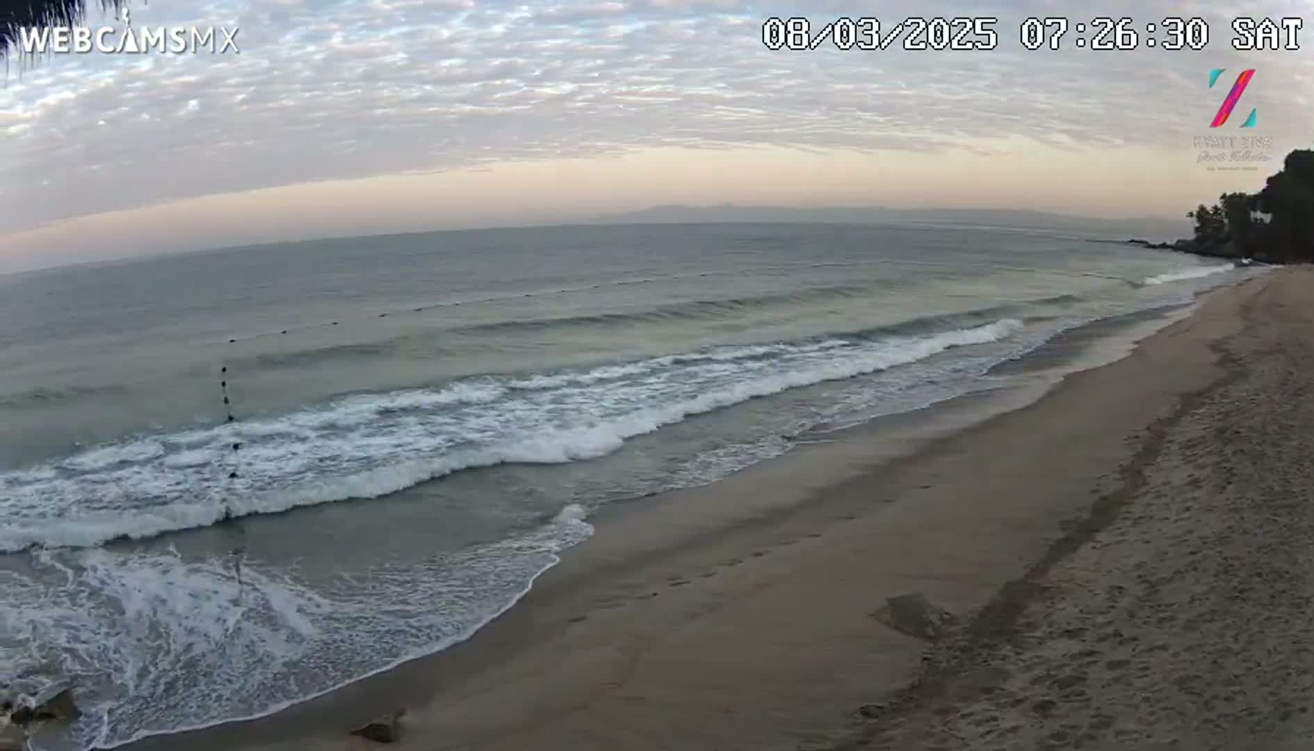A sandy beach with gentle waves rolling onto the shore under a cloudy, dawn sky.