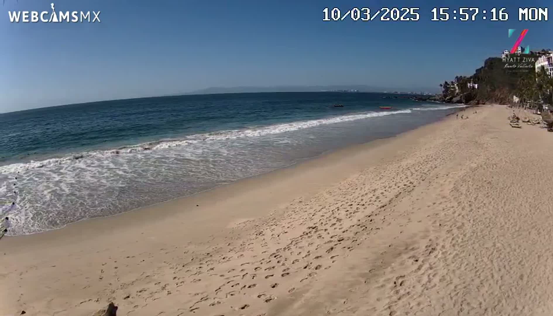 A sandy beach with small waves gently lapping the shore on a clear, sunny day.