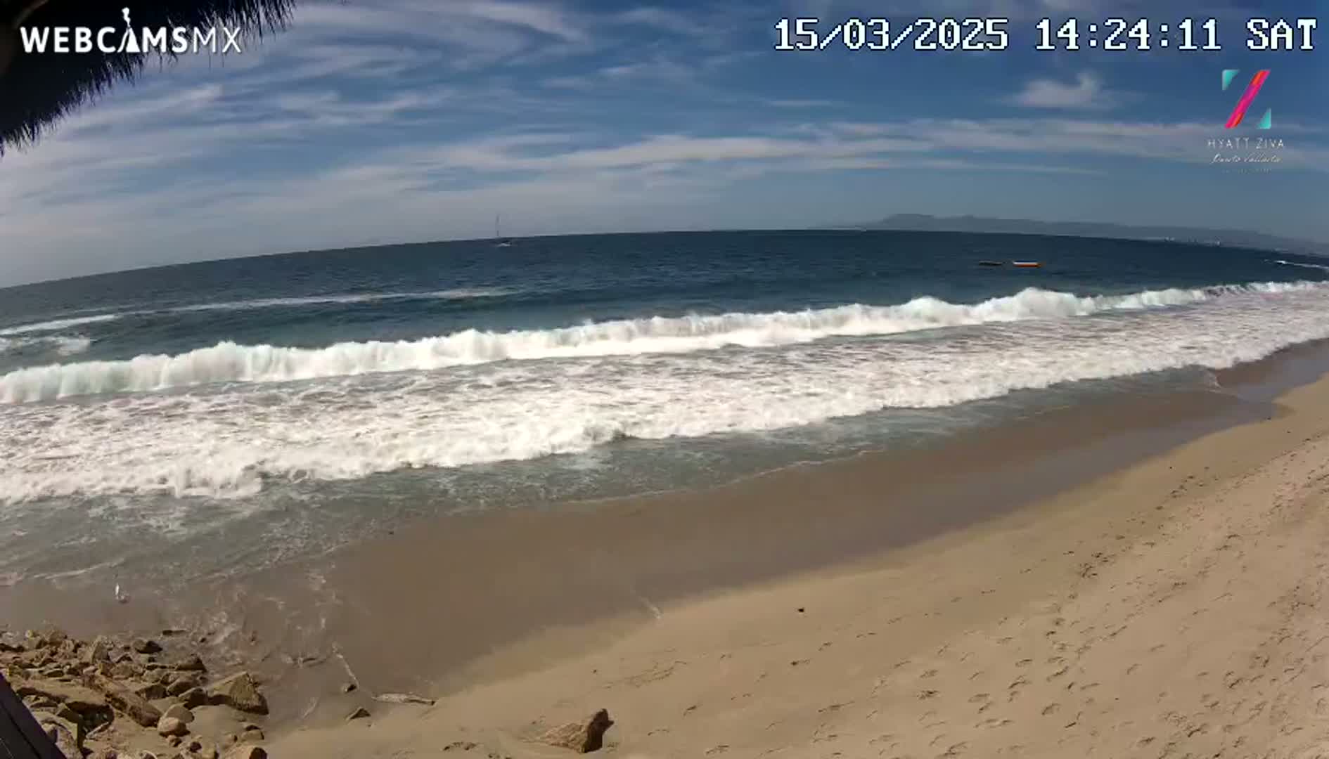 A sandy beach with gently rolling waves under a mostly sunny sky.