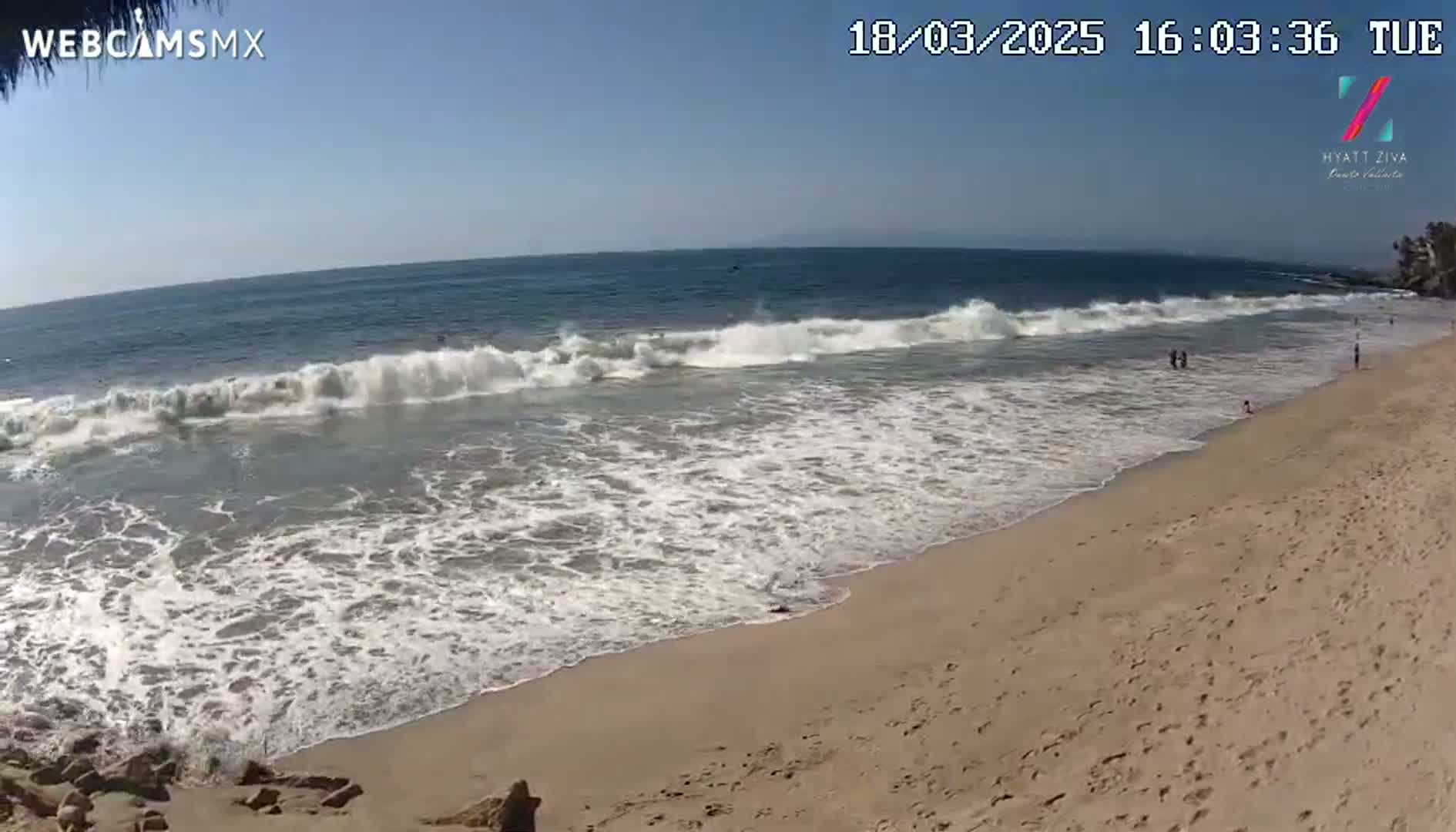 A sandy beach with moderate waves rolls onto shore on a sunny day.