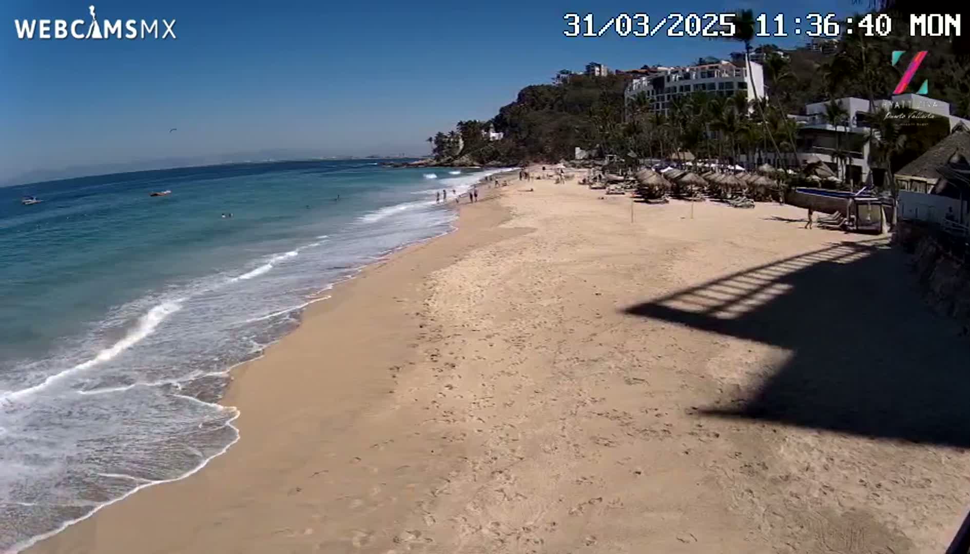 A sandy beach with calm, blue water and a few people on a sunny day.