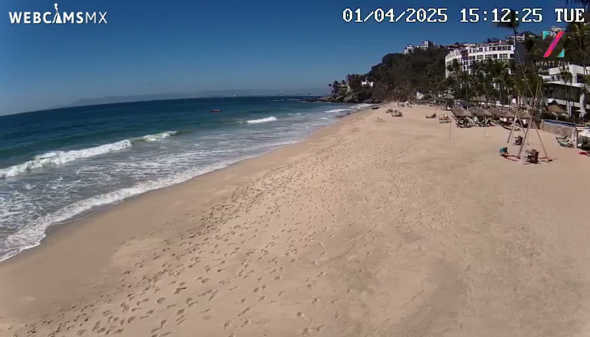 A sandy beach with footprints leading to calm ocean waves under a clear blue sky.