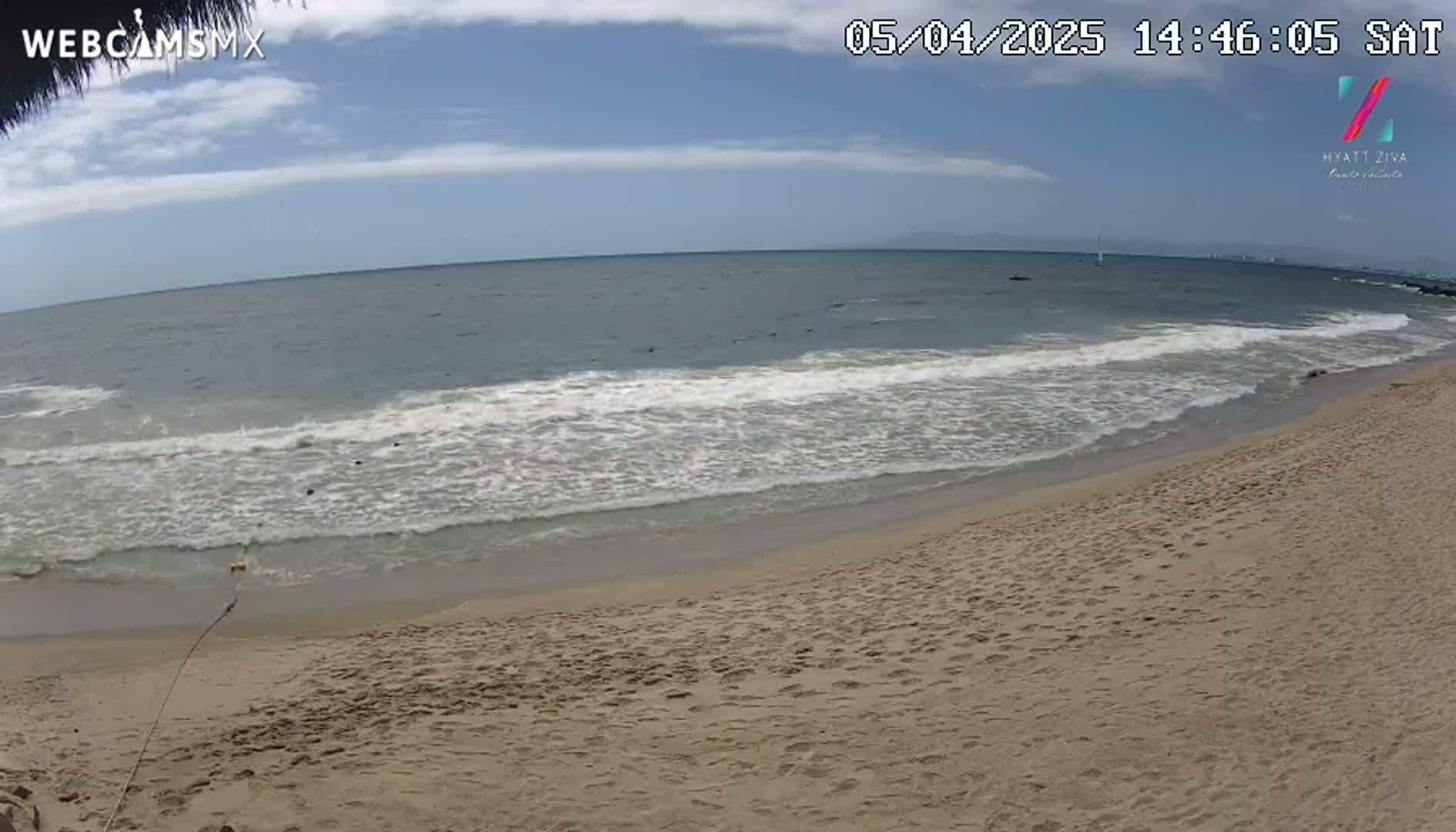 A sandy beach with gentle waves rolling onto the shore under a partly cloudy sky.