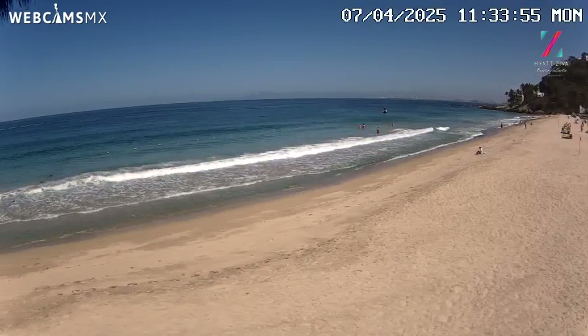 A sandy beach slopes gently down to a calm ocean under a clear blue sky.