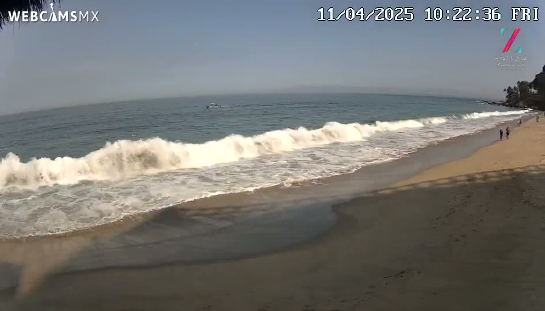 Ocean waves crash on a sandy beach under a clear, bright sky.