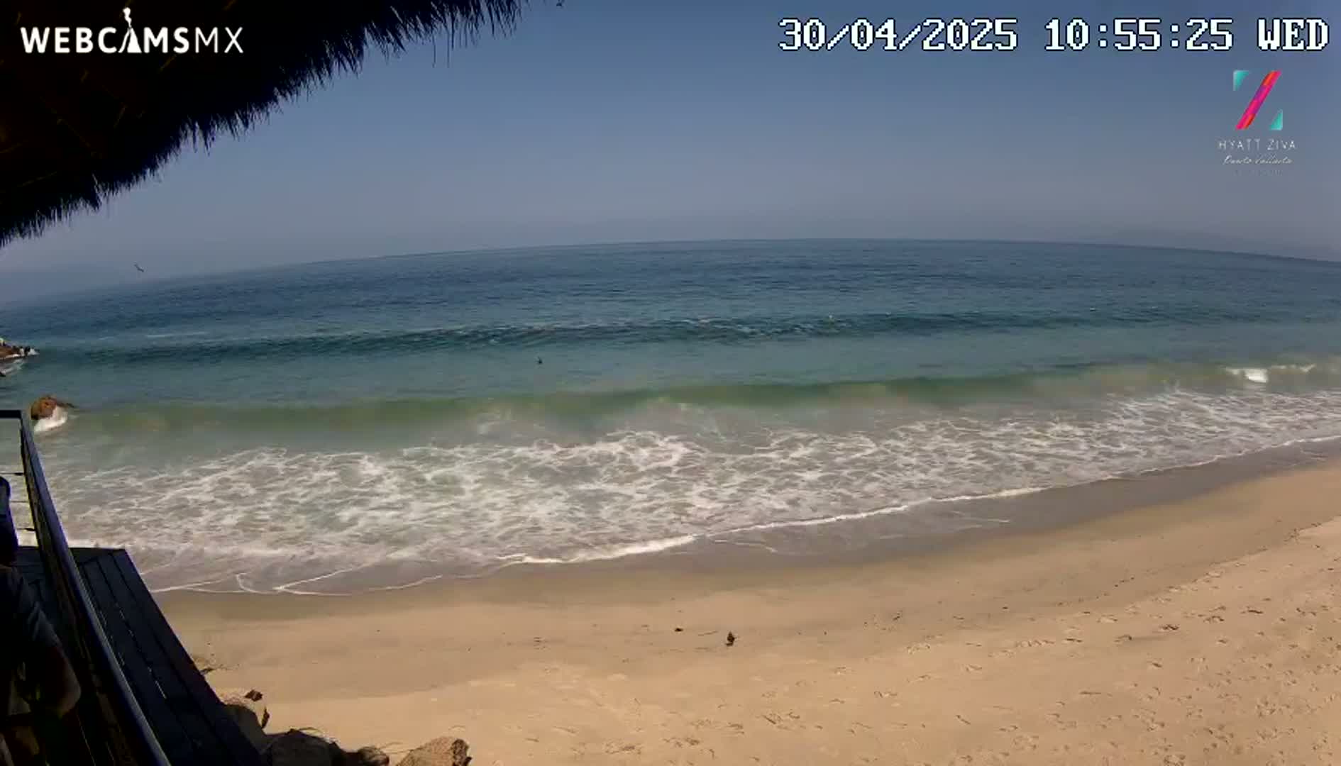 A sandy beach with gentle waves rolling onto the shore under a clear blue sky.