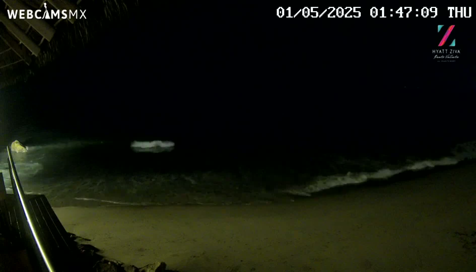 A nighttime beach scene shows gently lapping waves on a sandy shore, viewed from an elevated position on a deck.