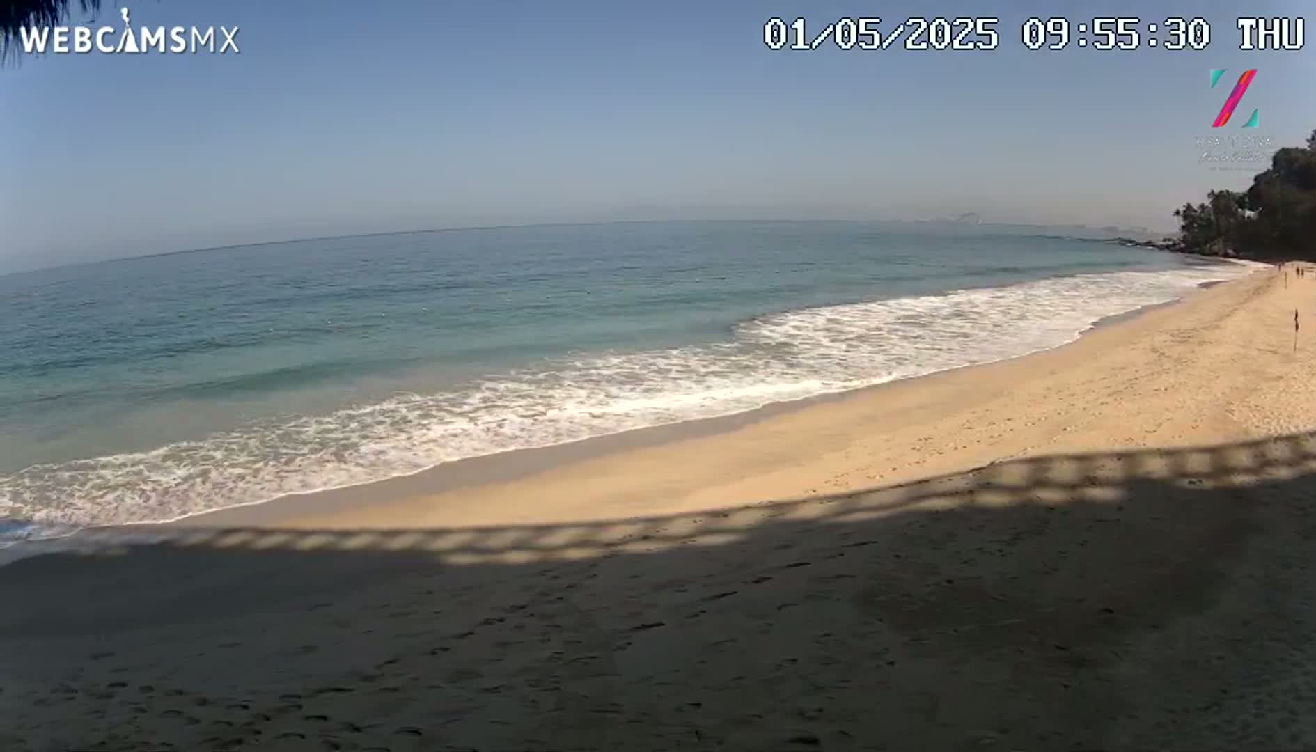 A sandy beach with gentle waves on a clear, sunny day.