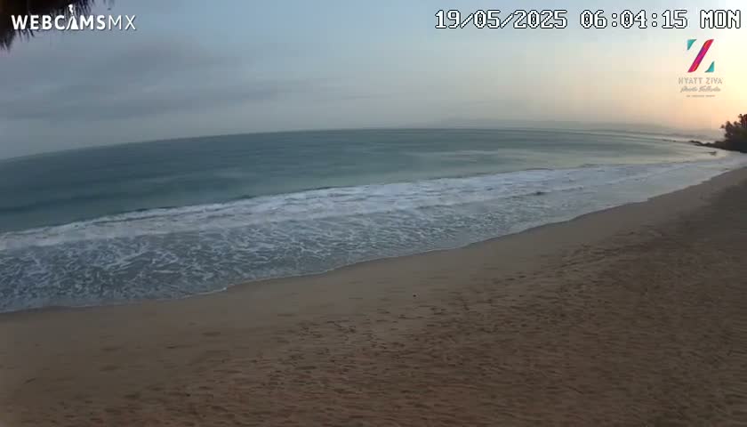 A sandy beach with gentle waves rolling onto the shore under an overcast sky.
