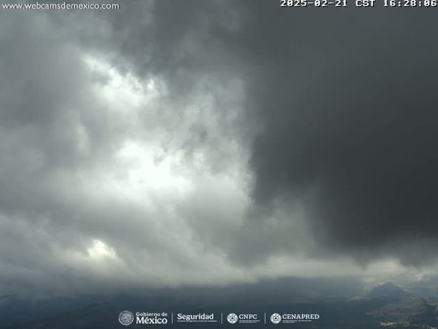 A mostly cloudy sky with dark, ominous clouds dominating the upper half of the frame, and lighter clouds and some sunlight breaking through in the lower half, overlooking a distant landscape.