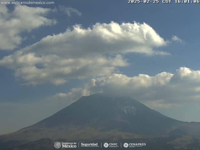 A partially cloudy sky overlooks a large, dark-colored volcano with a hint of snow near its peak.