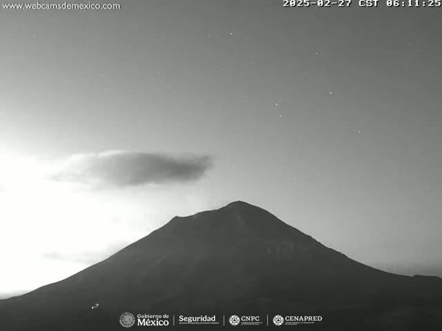 A dark, mountainous landscape is visible under a mostly clear night sky with a single, thin cloud.
