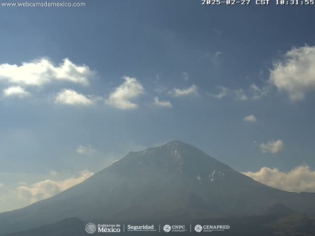 A snow-capped mountain is visible under a mostly clear sky with scattered clouds.
