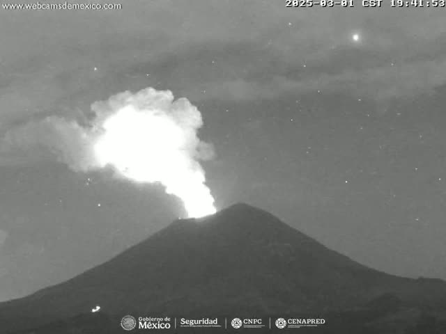 A nighttime, grayscale image shows a volcano erupting with a bright plume of smoke and ash against a starry sky.