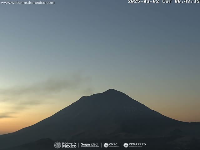 A large, dark volcano silhouetted against a twilight sky with a faint plume of smoke rising from its peak.
