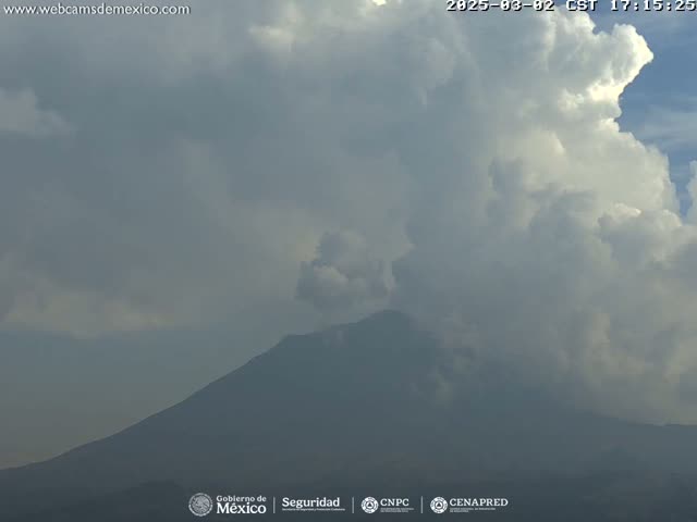 A large, dark mountain is partially obscured by a cloudy sky, with some areas of brighter clouds and hazy conditions.