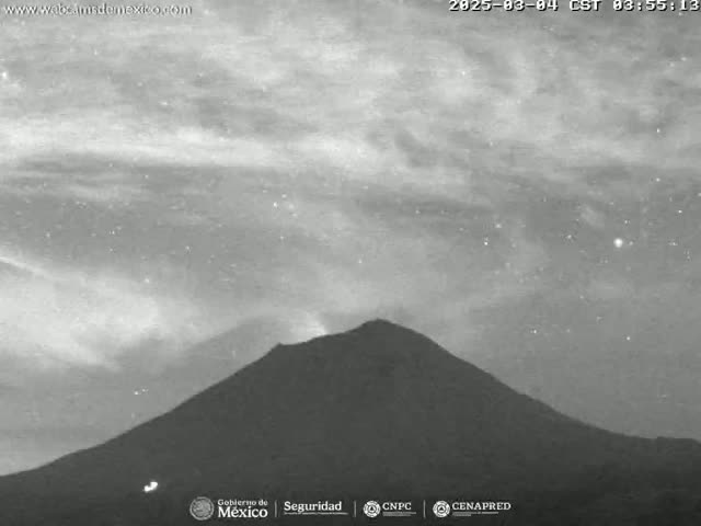 A large, dark mountain is silhouetted against a night sky with thin clouds and some visible stars.
