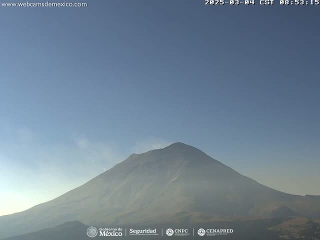 A large, dark mountain with a plume of smoke or steam rising from its peak is visible under a clear, light-blue sky.