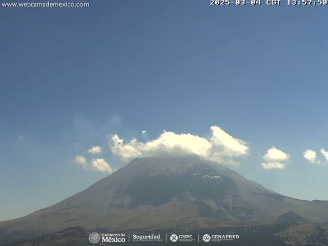 A large, dark-grey volcano is visible under a mostly clear sky with a few scattered white clouds.